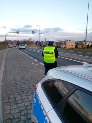 Policjant stoi obok radiowozu w zatoczce