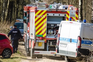 Policjanci idą obok wozu strażackiego, a w pobliżu stoi radiowóz