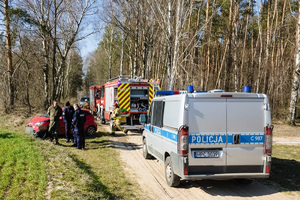 Policjanci i strażnik leśny stoją na skraju lasu, a w pobliżu wóz strażacki i radiowóz