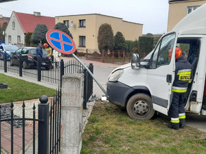 widok na bok samochodu dostawczego, który przewrócił znak drogowy na ogrodzenie posesji.