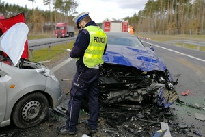 Policjant stoi przy rozbitych samochodach biorących udział w wypadku
