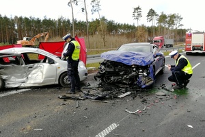 Dwóch policjantów stoi przy rozbitych samochodach biorących udział w wypadku