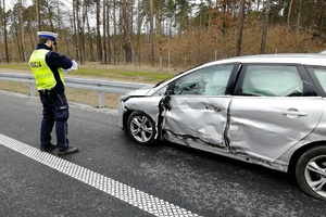 Policjant stoi przy rozbitym samochodzie biorącym udział w wypadku
