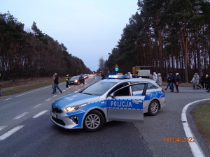 Widok na zaparkowany na drodze radiowóz i policjantów kierujących ruchem drogowym