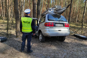Policjant stoi przy samochodzie rozbitym na drzewie
