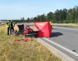 Widok na rozbity samochód i policjantów pracujących na miejscu wypadku