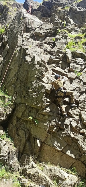 Alpinista wchodzący na pionową skałę z asekuracją, początek wejścia.