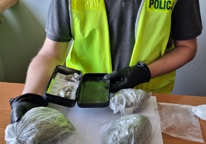 Policjant trzyma worek z marihuaną i metalowe pudełko z porcjami