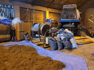 Wnętrze stodoły, worki leżą na podłodze, tytoń rozsypany i maszyna do krojenia