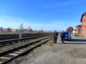 Policjanci idą wzdłuż torów w tle radiowóz i budynek dworca