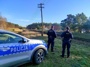 Policjanci stoją w pobliżu torów, obok nich radiowóz