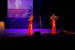 dwie kobiety ubrane w czerwone suknie grają na scenie na instrumentach muzycznych