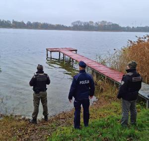 Policjant i strażnicy stoją nad brzegiem jeziora