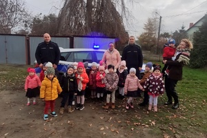 Dwóch umundurowanych policjantów z grupą dzieci, pozują na le radiowozu.