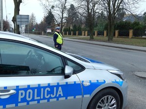 policjant stoi przy radiowozie i obserwuje ruch na drodze