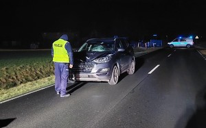 Policjant stoi przy rozbitym samochodzie biorącym udział w wypadku