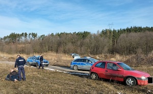 Policjanci stoją nad uciekinierem w pobliżu zaparkowane są radiowozy i samochód zatrzymanego