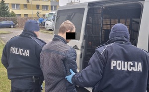 dwóch umundurowanych policjantów prowadzi zatrzymanego skutego kajdankami do radiowozu