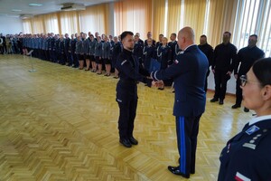 Komendant Wojewódzki Policji w Bydgoszczy gratulując uściska rękę policjantowi i podaje niebieską teczkę