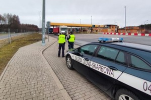 policjant i funkcjonariusz Krajowej Administracji Skarbowej stoją obok siebie przy radiowozie Krajowej Administracji Skarbowej