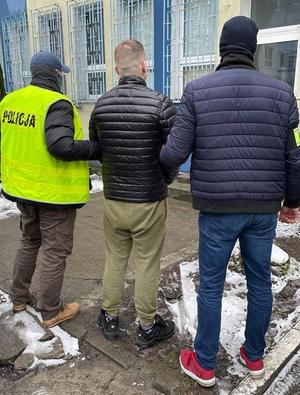 dwaj policjanci trzymają zatrzymanego skutego kajdankami zespolonymi