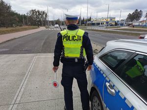 Policjant stoi przy radiowozie i obserwuje ruch drogowy przy przejściu dla pieszych