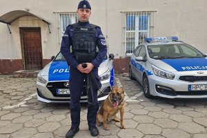 umundurowany policjant pozuje do zdjęcia z psem służbowym na tle radiowozu