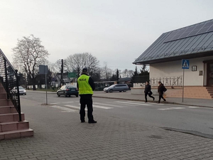 Policjant stoi przy przejściu dla pieszych i obserwuję przechodzące przez jezdnię osoby