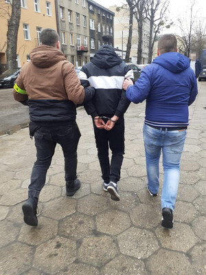 dwaj nieumundurowani policjanci prowadzą zatrzymanego skutego kajdankami założonymi na ręce trzymane z tyłu