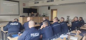 Policjanci i wykładowca w sali wykładowej podczas szkolenia, widok z tyłu sali.