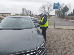 policjant sprawdza dokumenty kierowcy przy zatrzymanym do kontroli samochodzie