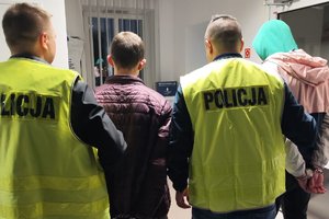 dwaj policjanci trzymają dwóch zatrzymanych skutych kajdankami