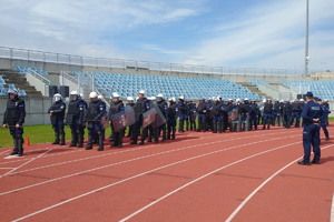 policjanci stoją w drużynach na płycie stadionu ubrani w sprzęt ochrony osobistej