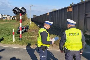 Dwaj policjanci RD sporządzają dokumentację, w tle rozbite auto, a obok pociąg towarowy