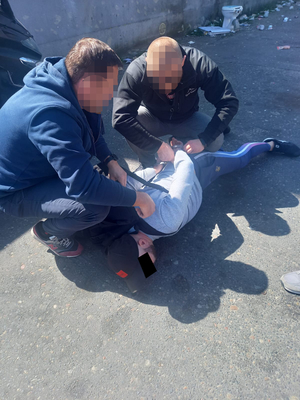 policjanci kucają nad zatrzymanym mężczyzną leżącym na ziemi i zakładają mu kajdanki na ręce