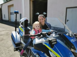 Policjantka stoi przy policyjnym motocyklu na którym siedzi dziewczynka