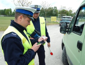 Policjant RD weryfikuje dane kontrolowanego kierowcy, obok stoi drugi policjant, a w tle auto m-ki Kia