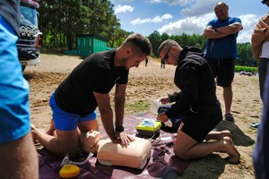 dwóch mężczyzn klęczy nad manekinem i przeprowadzają reanimację