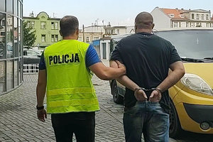 policjant prowadzi zatrzymanego skutego kajdankami założonymi na ręce trzymane z tyłu
