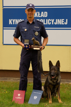 Policjant z psem  prezentuje nagrody.