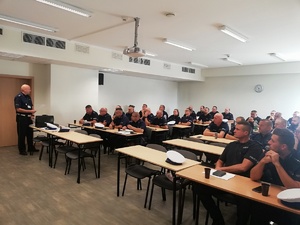 widok na policjantów uczestniczących w szkoleniu siedzących przy stołach na sali wykładowej