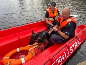 policjant wraz z psem i strażakiem siedzą na łodzi