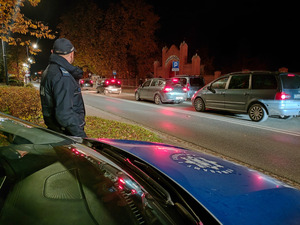 Policjant przy radiowozie w okolicach cmentarza.