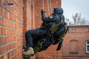 Policyjni kontrterroryści na linach  przy murze.