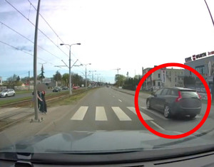Kierowca auta zaznaczonego w czerwone kółko popełnia wykroczenie. Przejeżdża przez przejście pomimo, że inny pojazd zatrzymał się, bo nadchodzą piesi.