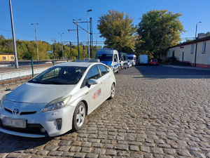 Radiowóz policji i inne samochody służb mundurowych zaparkowane przy samochodzie z napisem taxi