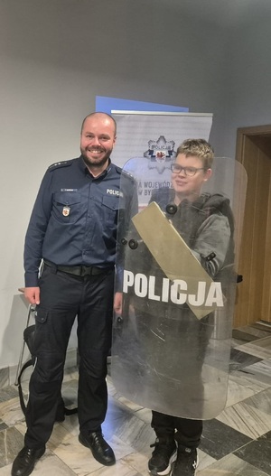 Policjant pozuje do zdjęcia z młodym mężczyzną trzymającym tarczę policyjną