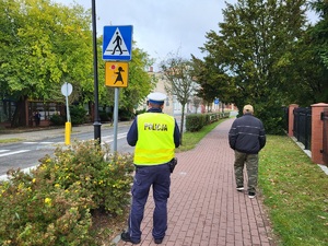 Policjant stoi na chodniku i obserwuje ruch na przejściu dla pieszych