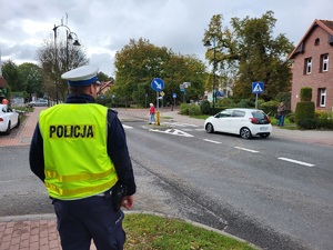 Policjant stoi na chodniku i obserwuje ruch na przejściu dla pieszych