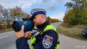 Policjant stoi przy drodze i mierzy prędkość